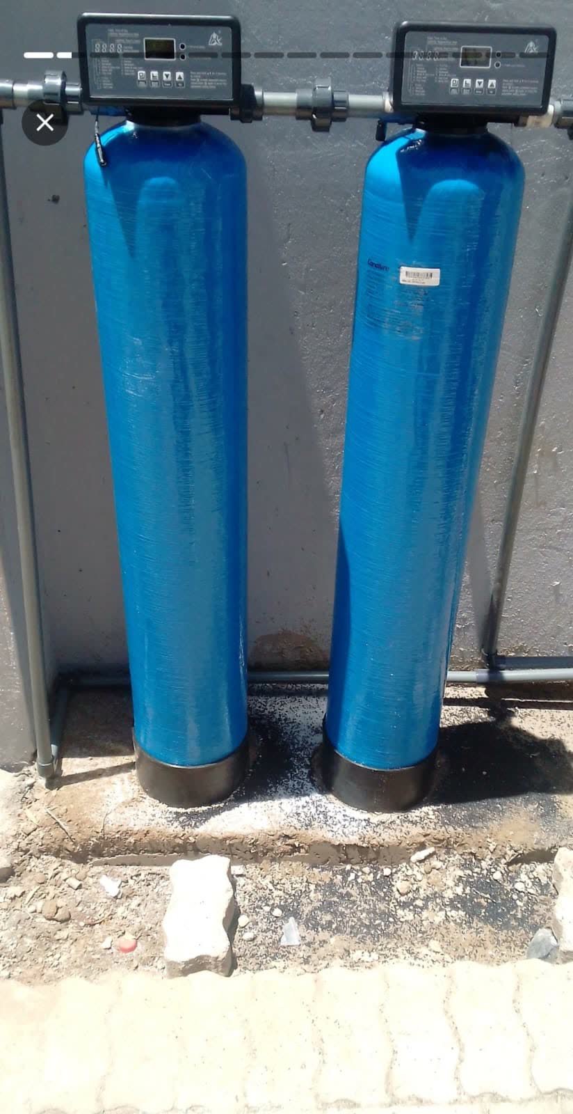 Twin blue water filtration vessels with digital control heads installed against a wall